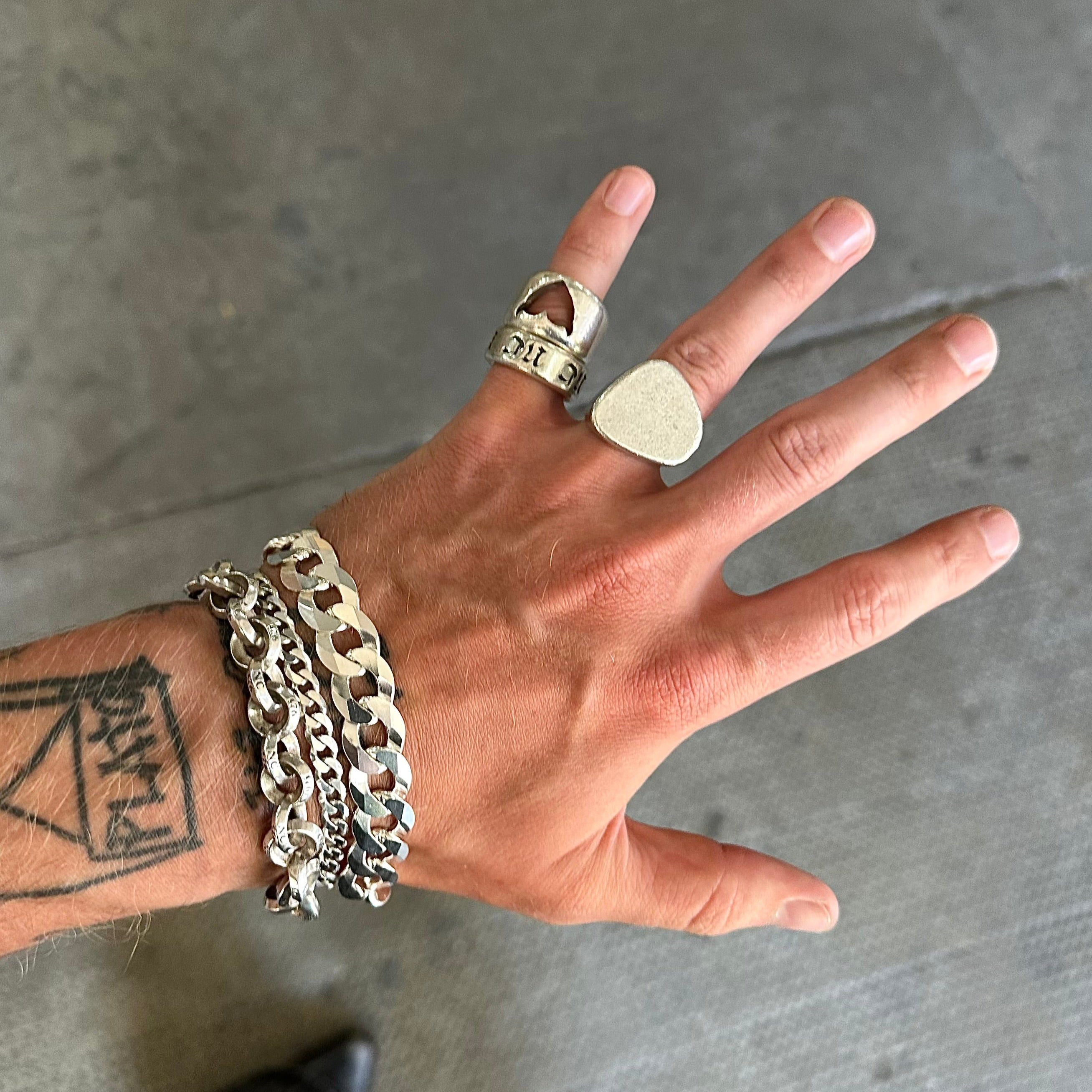 Hand wearing multiple rings and a bracelet on a gray concrete floor