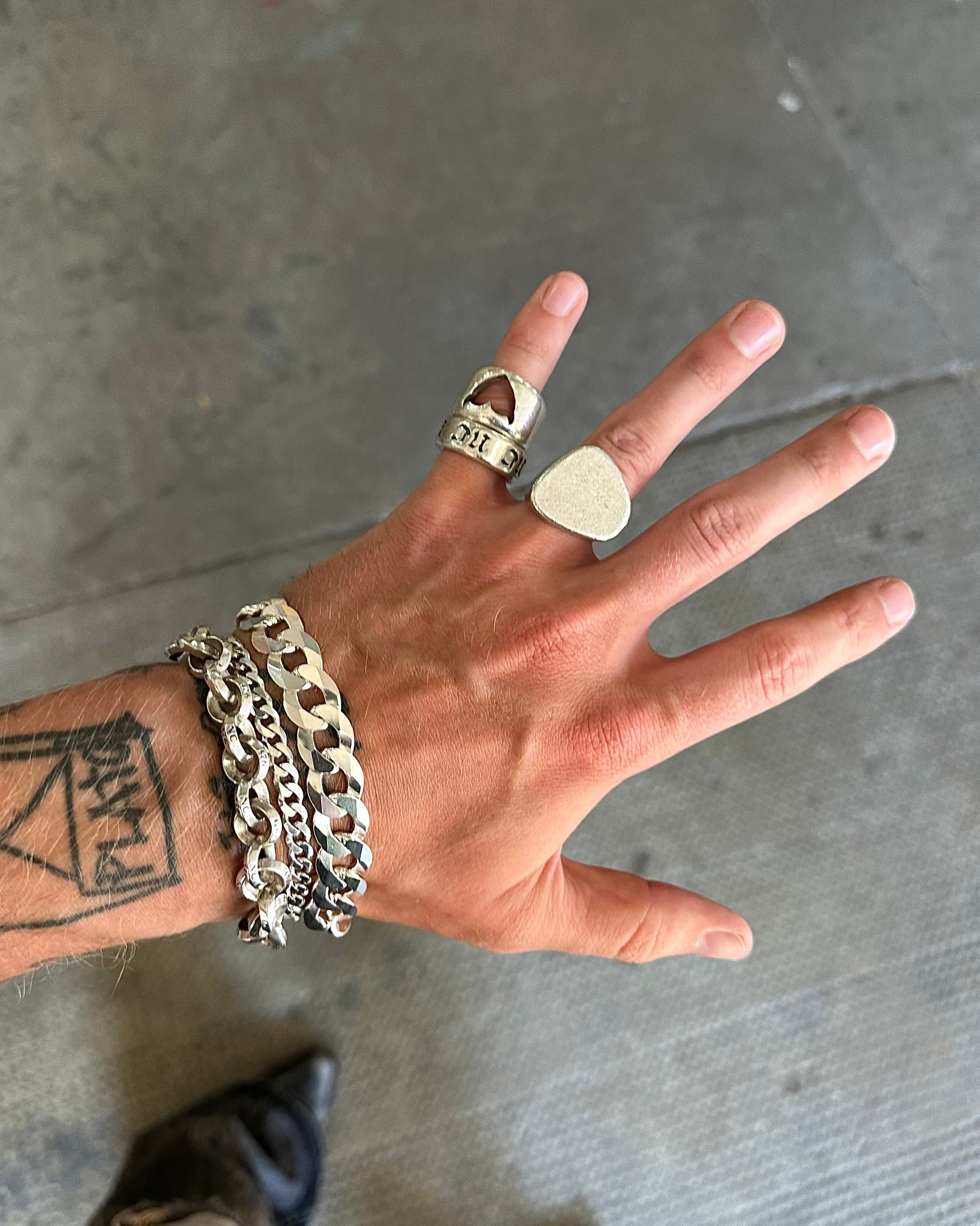 Hand wearing multiple rings and a bracelet on a gray concrete floor